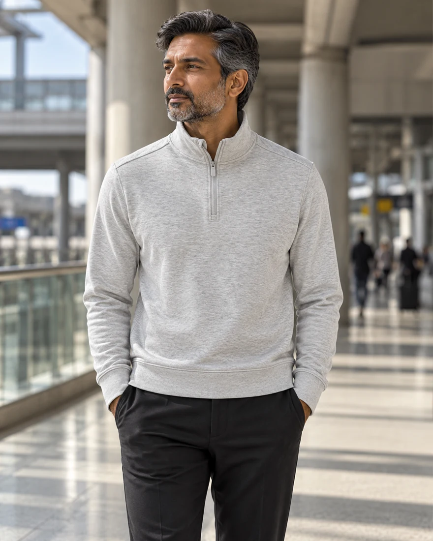 A grey-haired man in the heather Quarter Zip standing in an airport terminal
